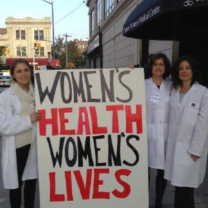 Volunteers hold sign outside Choices stating Women's Health Women's Lives